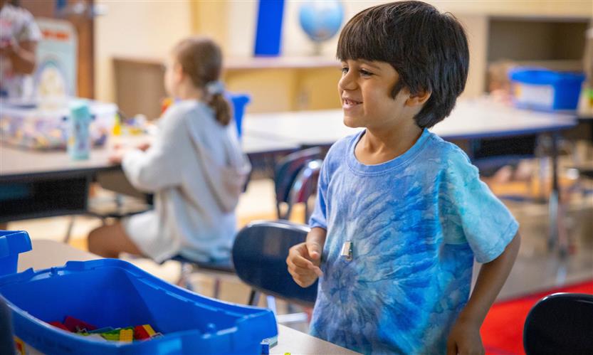 A boy wearing a blue shirt smiles while playing with legos